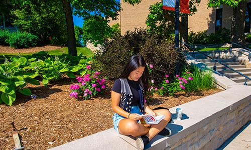 a Carroll University student sitting on a ledge reading a book.